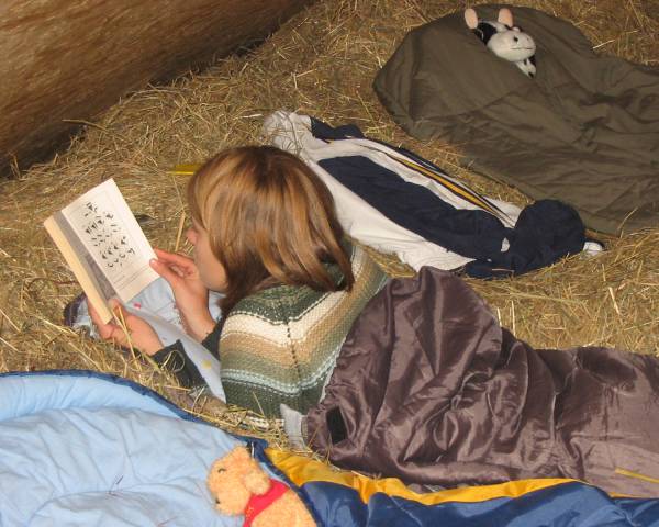 Kind im Schlafsack liegt im Heu und liest ein Buch